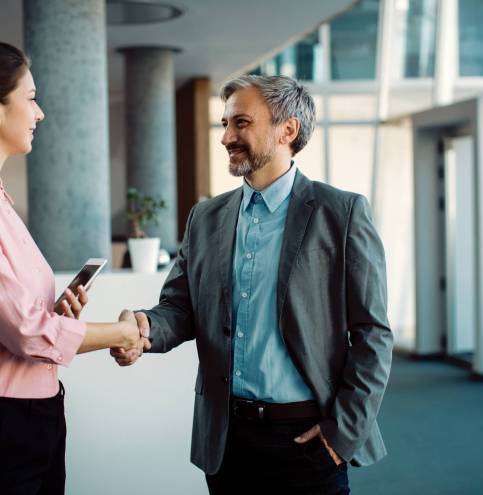 Happy businessman handshaking with female coworker while greeting in a lobby.